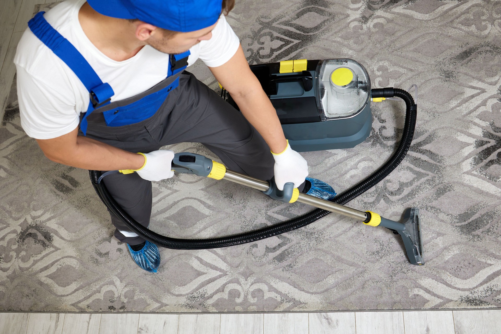 Professional cleaning service worker in uniform using a vacuum cleaner on a carpet