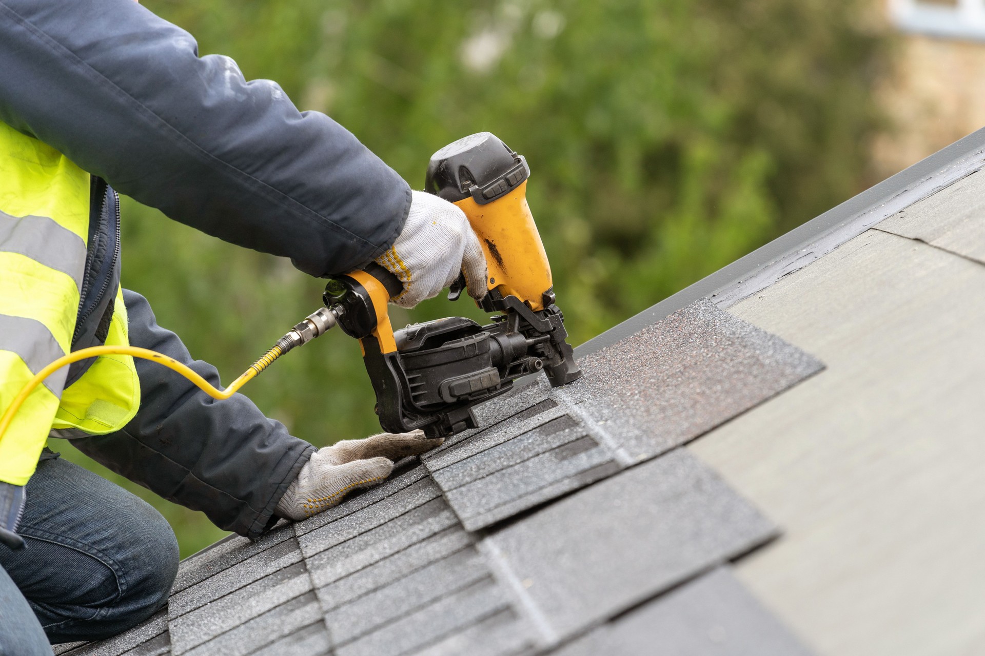 Workman using pneumatic nail gun install tile on roof of new house under construction