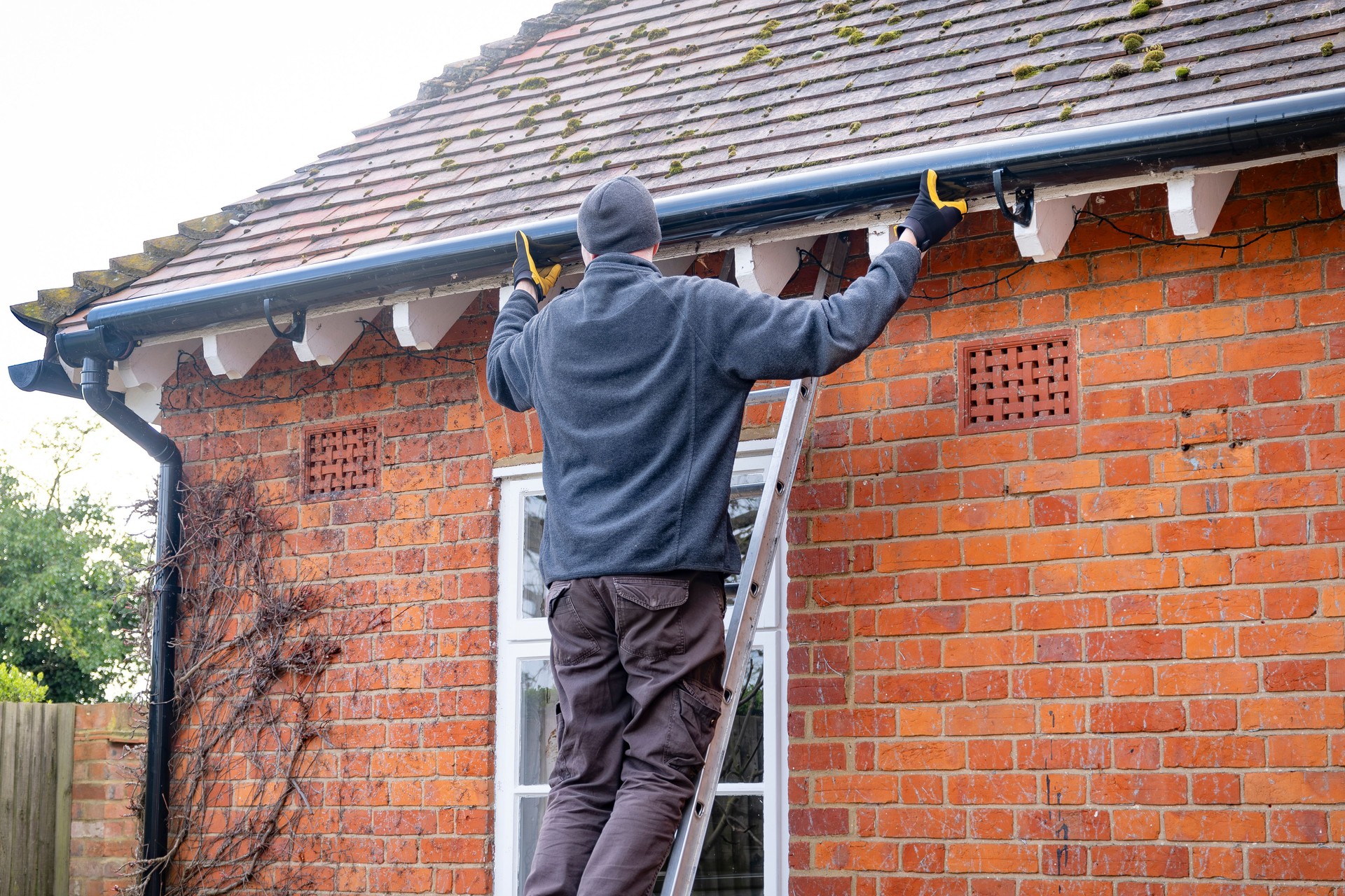 Man on a ladder fixing rain gutter on a UK house