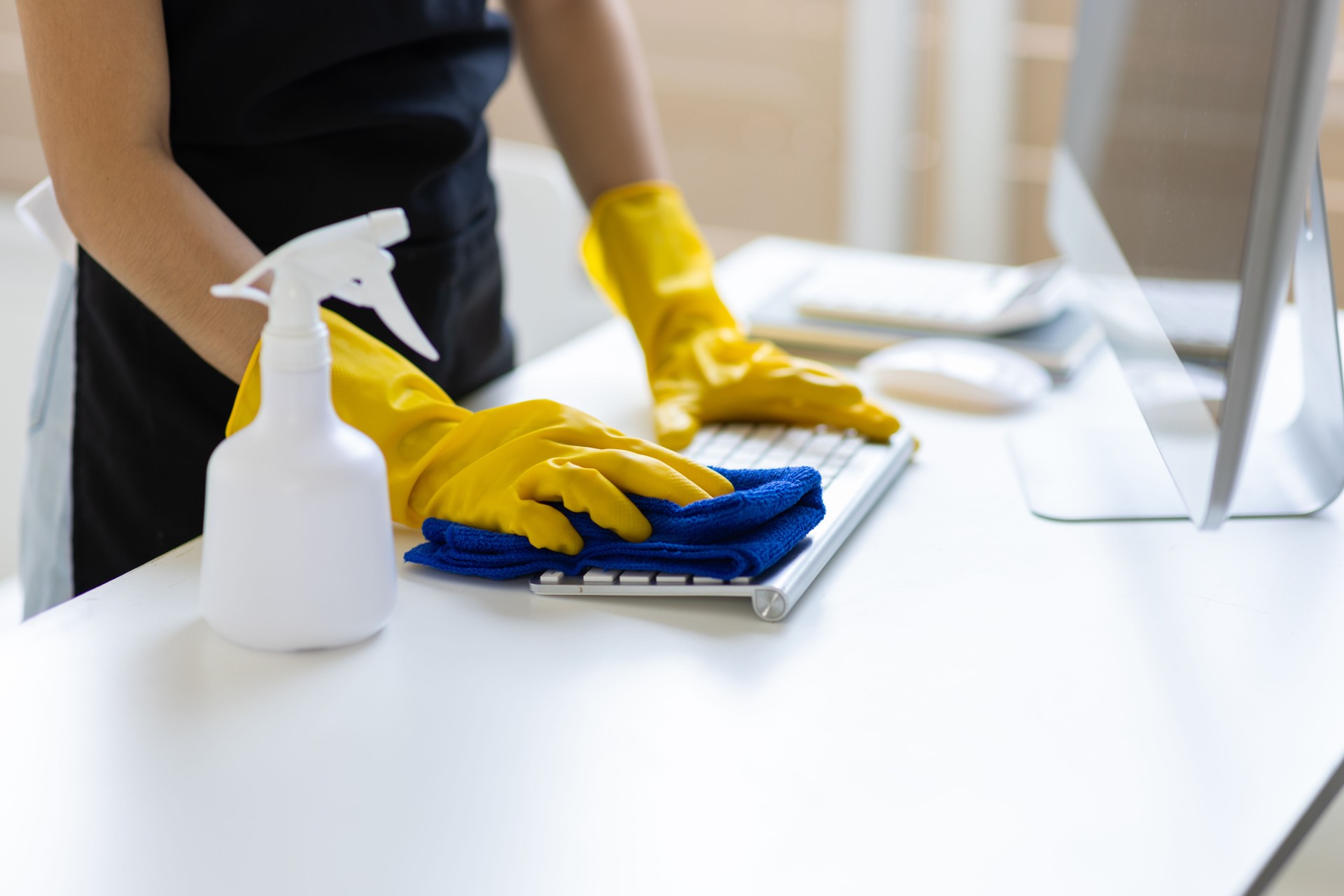 Young Asian cleaning woman uses a towel to clean a computer using cleaning solution in her home office.